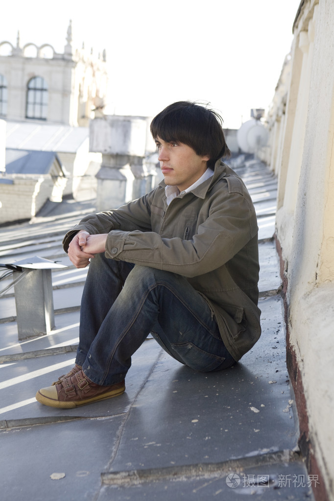 年轻严重英俊的男人坐在屋顶上