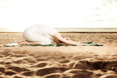 年轻漂亮苗条的女人练瑜伽母在沙滩上