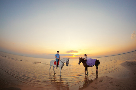 日落海滩上马背上的两个车手。爱好者骑开胃