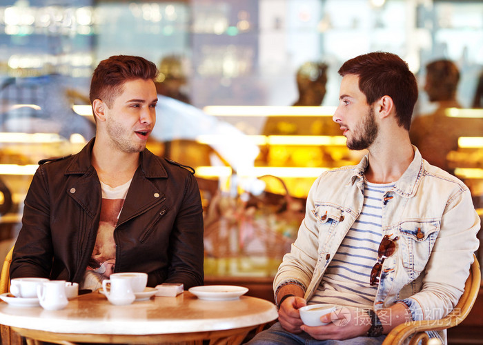 两个年轻时髦的家伙坐在咖啡厅聊天，喝咖啡微笑