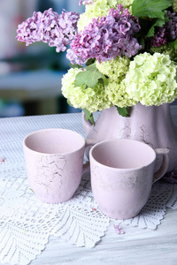 组成与茶杯子和美丽的春天鲜花插在花瓶里，木制的桌子，在明亮的背景上