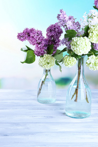 在玻璃瓶，木制的桌子，在明亮的背景上的美丽的春天的花朵