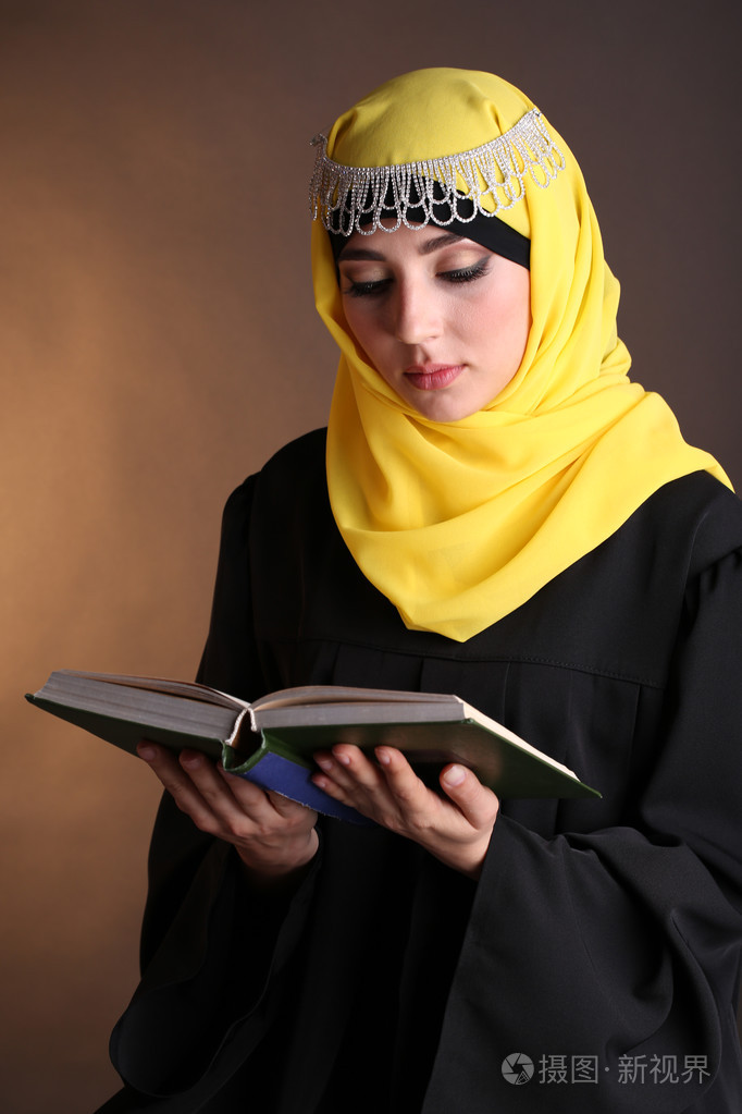 穆斯林阿拉伯语美女在深色背景上的书