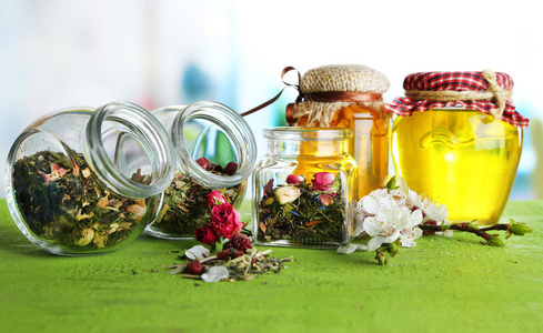 各式各样的草药和茶在玻璃罐里的木桌前，在明亮的背景上