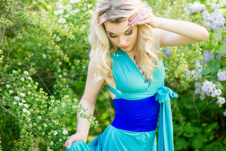 美丽年轻的金发女郎与长长的头发在长长的蓝色的连衣裙在自然高衩的肖像