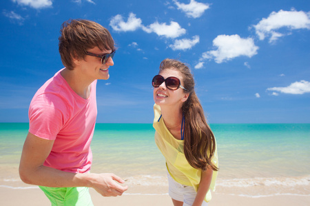 在明亮的衣服和太阳镜在地处热带的海滩上尽情的快乐年轻夫妇的肖像