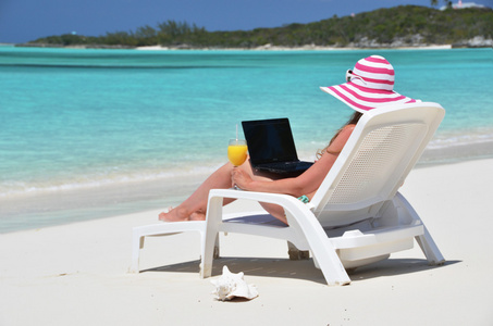 用一台笔记本电脑在热带海滩上的女孩