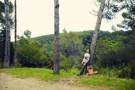 年轻的徒步旅行者背包小木材山上休息靠在一棵树