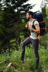 年轻的旅行者，站在小山上的森林里，看着别处，背包里