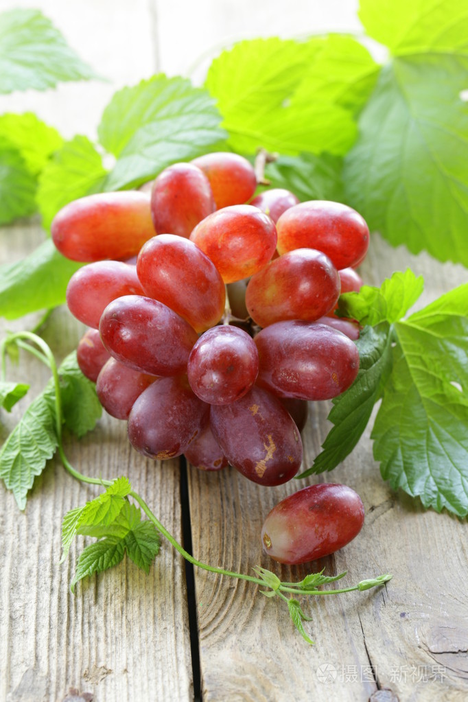 红色熟透的葡萄,绿色的叶子,木制的桌子上的分支