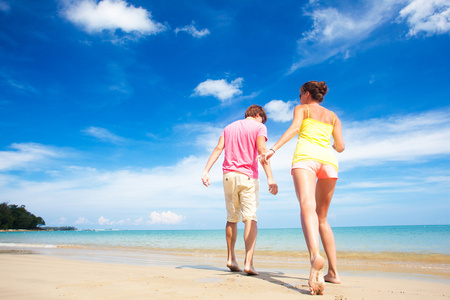 在明亮的衣服和太阳镜在地处热带的海滩上尽情的快乐年轻夫妇的肖像
