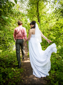 新郎和新娘穿白色长礼服，走在森林中