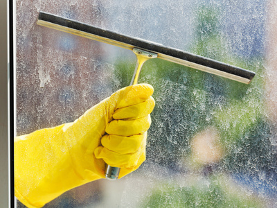 在黄色的手套的手洗窗口由刮板