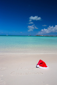 写在热带海滩白色沙子与圣诞帽子上的圣诞快乐