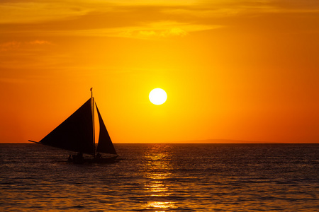 在日落时在热带海洋上的帆船。剪影照片