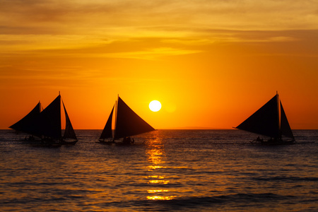 在日落时在热带海洋上的帆船。剪影照片