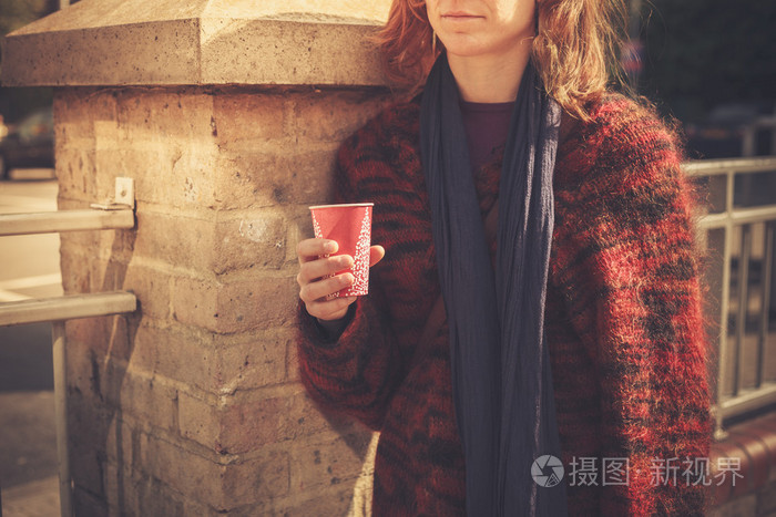 年轻的女子站在街与一个纸杯
