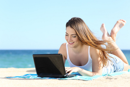 快乐少女浏览社交媒体在海滩上的一台笔记本电脑
