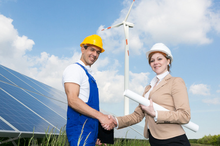 在太阳能电池板和风力发电机组的工程师握手