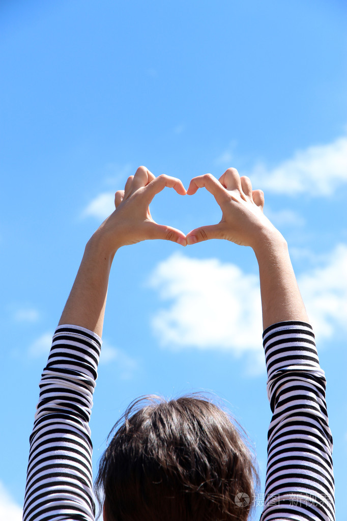 年轻的女孩抱着双手在蓝色的天空背景心形状边框