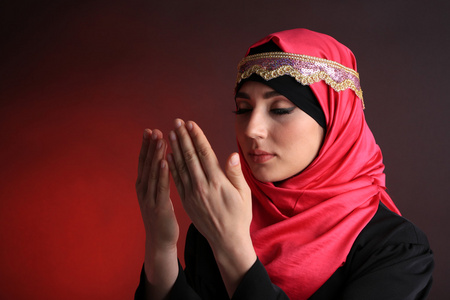 穆斯林阿拉伯语美女在深色背景上祈祷照片