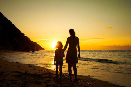 母亲和女儿在日出时在海滩上玩