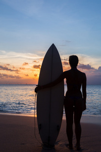 女人的冲浪者，以在日落时分的热带海滩上的冲浪板