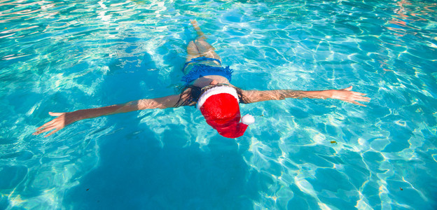 在蓝色的水面上后视图的美丽的女人，在圣诞老人的帽子