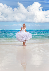 在新娘的礼服的年轻漂亮的女人在海浪上运行