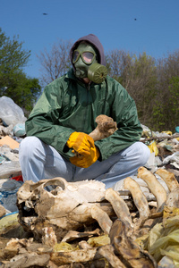 坐在垃圾上，拿着一根骨头的防毒面具的人