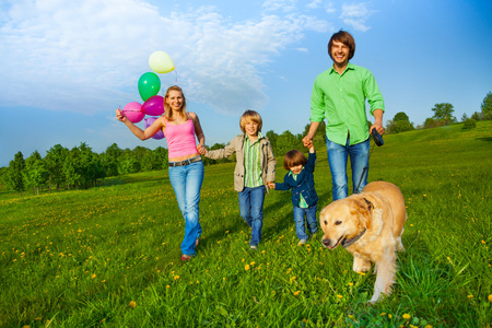 幸福的家庭与气球和狗在公园散步