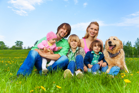 微笑家庭坐在绿草与狗