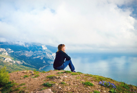 年轻的女孩坐在小山上，俯瞰着大海