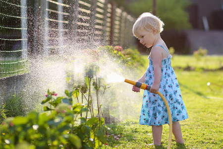 可爱的小女孩在花园里使用喷雾软管浇水
