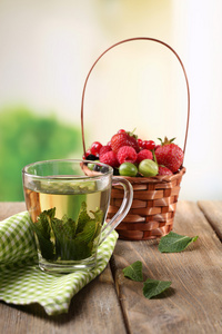森林莓果在柳条篮子和玻璃杯薄荷茶，木制的桌子，在明亮的背景上