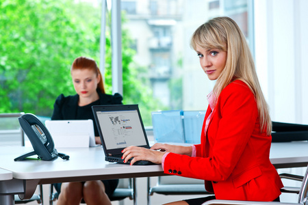 业务 womanworking 与背景的同事的笔记本电脑上
