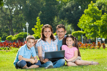 幸福的家庭使用的便携式计算机放在草地上