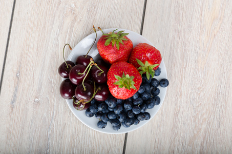 蓝莓，樱桃和草莓在木制的桌子上的小盘子上