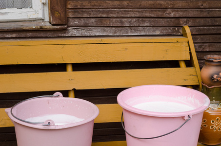 木长凳上的两桶粉红色的桶满鲜牛奶