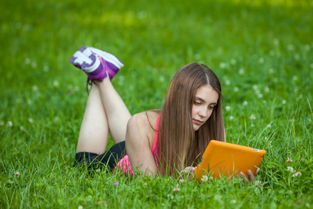 美丽的年轻女子坐在公园的平板电脑