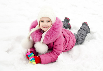 可爱微笑的小女孩躺在雪地上在冬季的一天