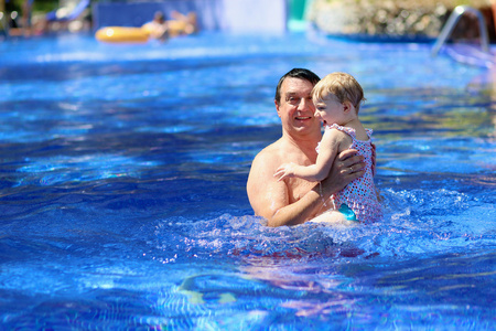 快乐的父亲和在户外游泳池玩乐的小女儿