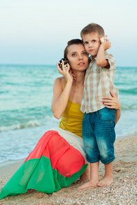 年轻的母亲和她的儿子在沙滩上的贝壳