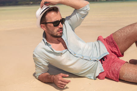 性感的男人,在沙滩拿着帽子和视线上照片