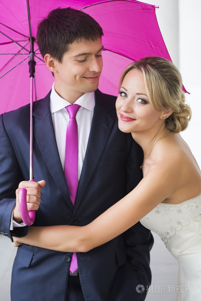 粉红色的雨伞的结婚礼服的年轻夫妇拥抱