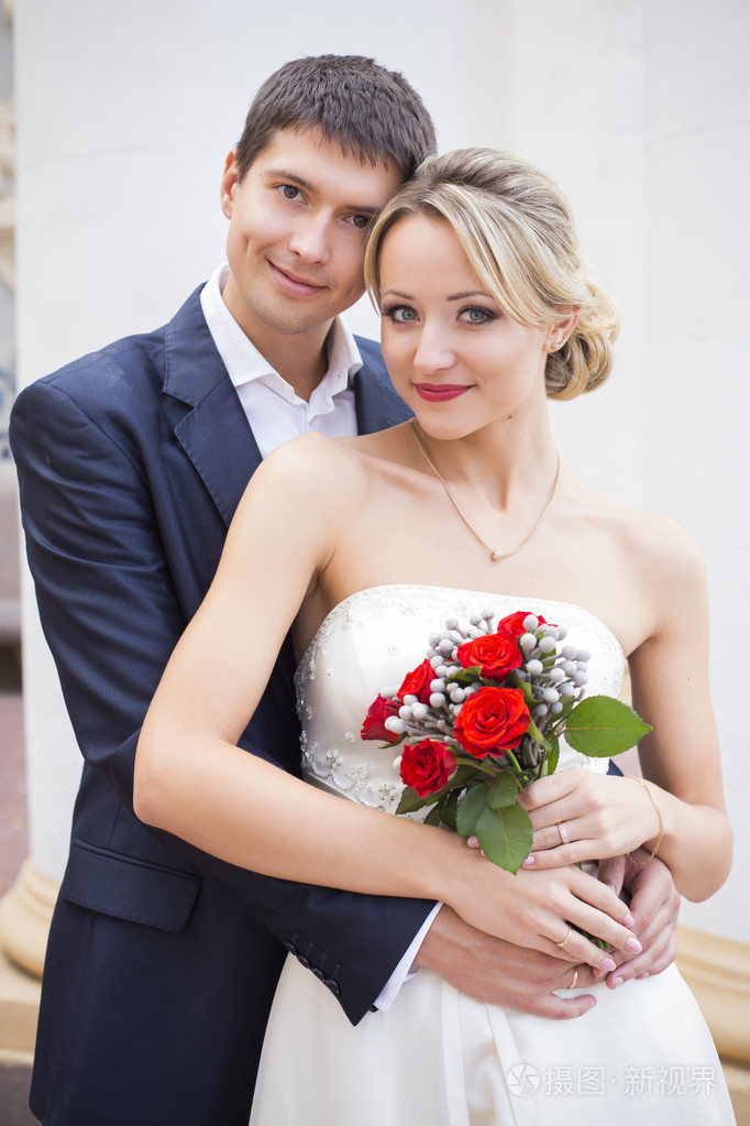 接吻的结婚礼服的年轻夫妇.新娘紧握着红玫瑰花束