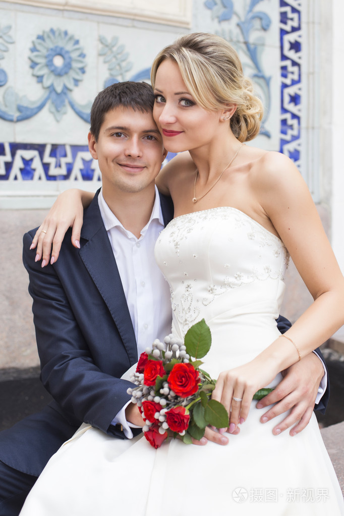 接吻的结婚礼服的年轻夫妇新娘紧握着红玫瑰花束