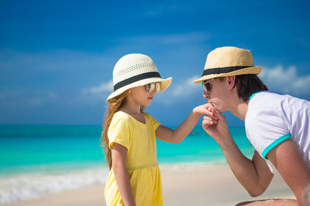 快乐爸爸亲吻他在海滩上的小女儿的手
