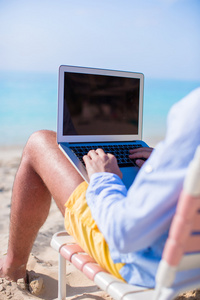 在地处热带的海滩在笔记本电脑上工作的年轻人