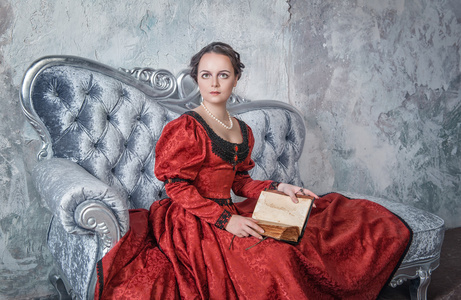 在沙发上用书中世纪穿着美丽的女人